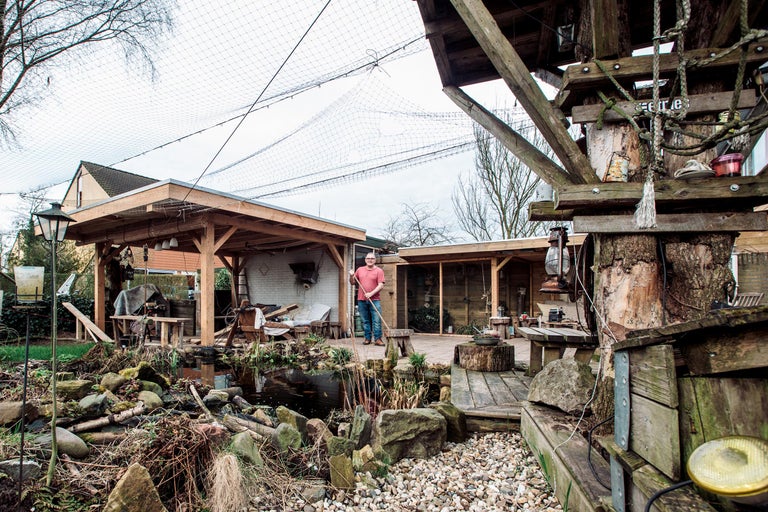 Tuin met vijver, tuinhuis, vogelnet en een man met hark.