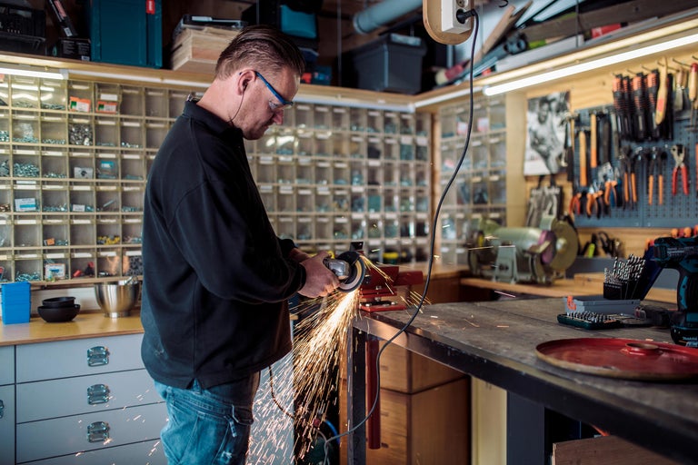 Ambachtsman in werkplaats met haakse slijper die metaal slijpt