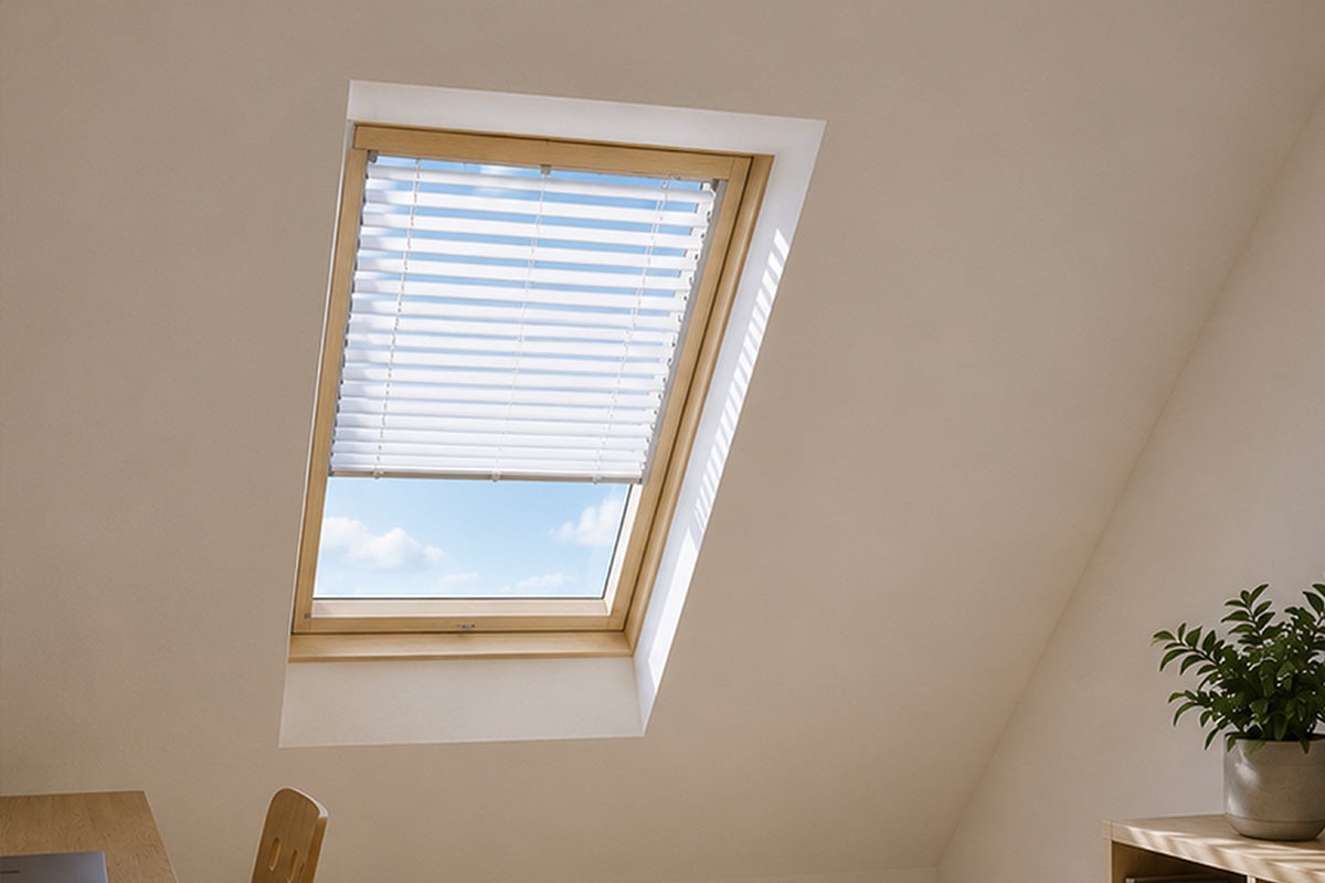 Dakraam van hout met witte jaloezie in een lichte zolderkamer met zicht op de blauwe lucht.