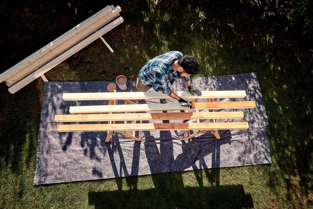 Man schildert houten planken in de tuin met houtbeschermingsbeits op een werkbank