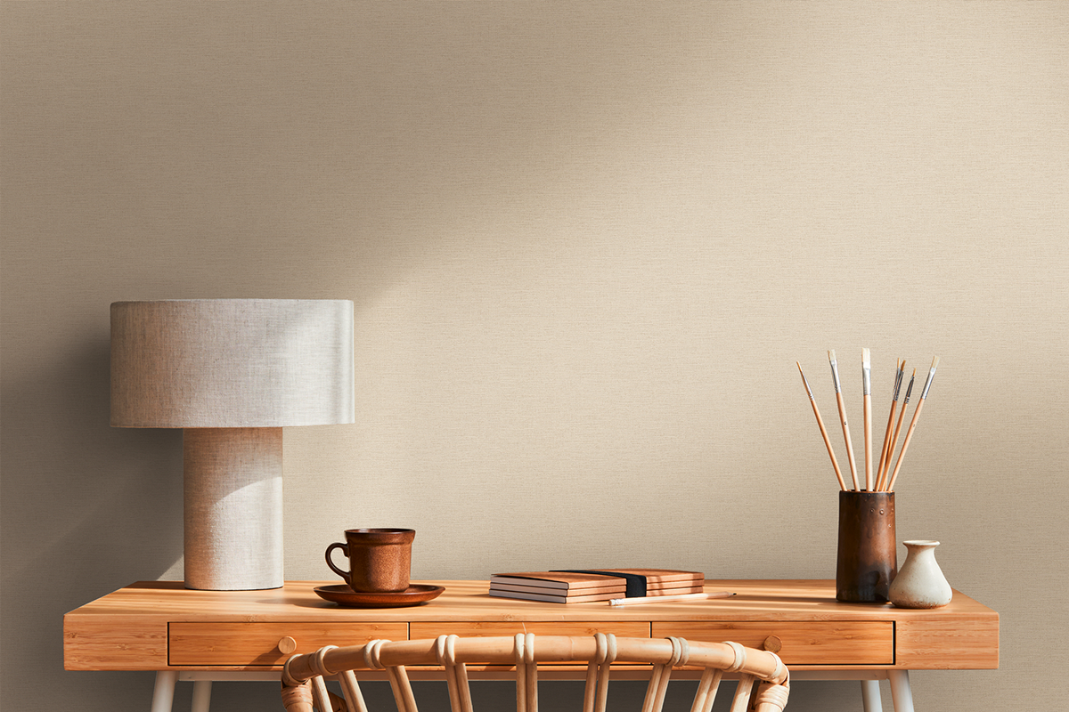 Gestructureerd behang achter een houten bureau met stoffen lamp, notitieboekjes en penselen in een lichte, opgeruimde kamer.