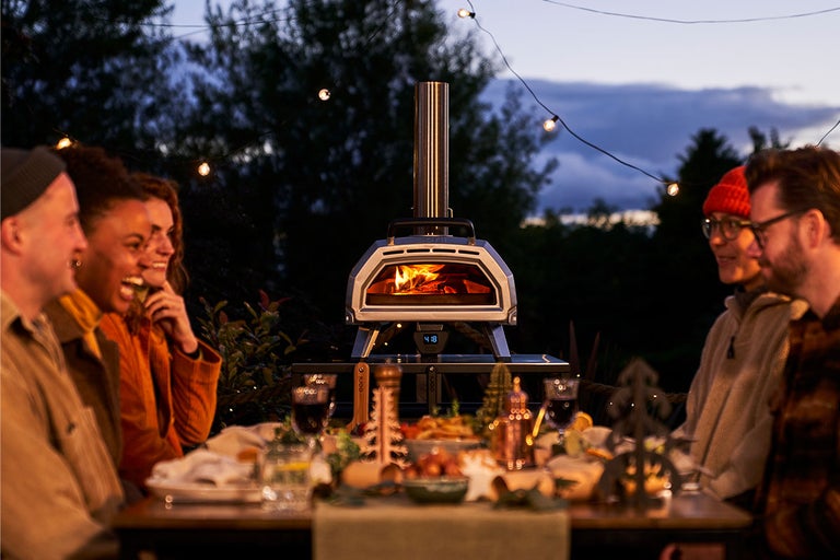 Groep mensen zit 's avonds buiten aan een tafel met een pizzaoven