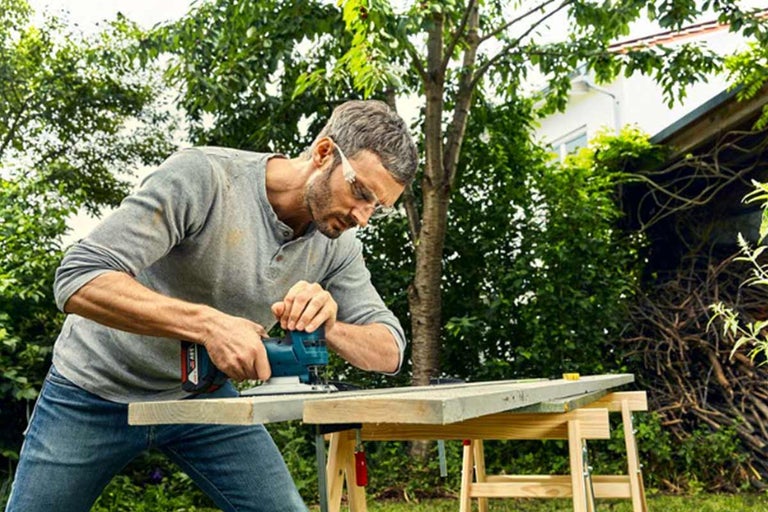 Man schuurt een houten plank met een multislijper buiten