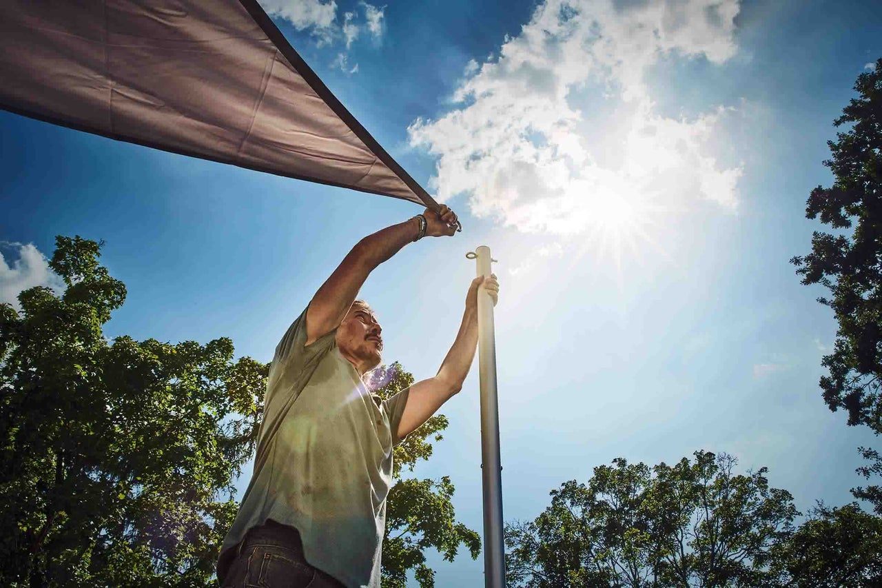 Een man bevestigt een schaduwdoek aan een metalen paal in de tuin bij zonnig weer.