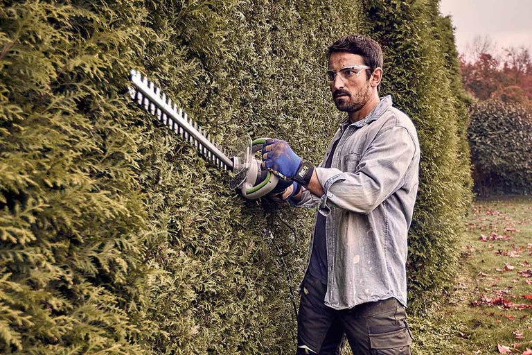 Een man snoeit een heg met een heggenschaar.