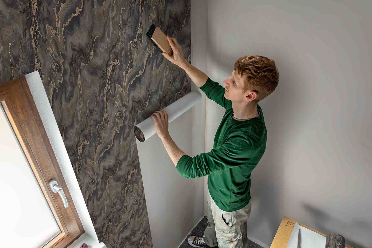 Een man behangt een muur met een behang met marmerpatroon.