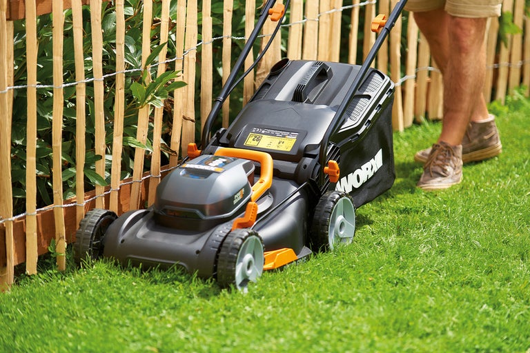 Worx grasmaaier op een gazon voor een houten schutting