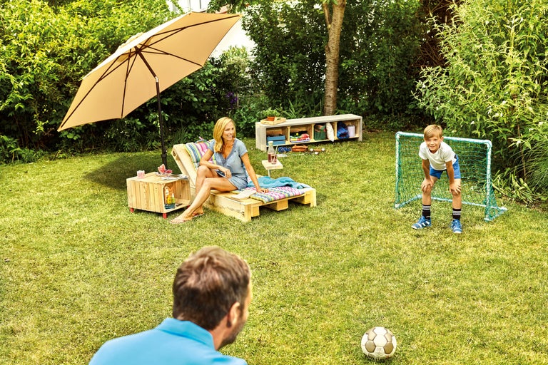 Scene in de tuin met parasol, ligstoel van houten pallets, jongen en voetbaldoel