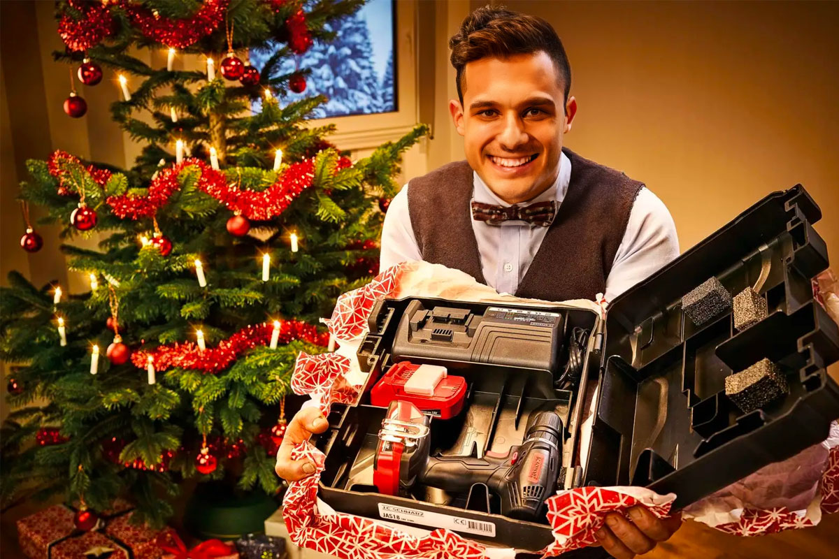 Man presenteert boormachineset als kerstcadeau voor een kerstboom