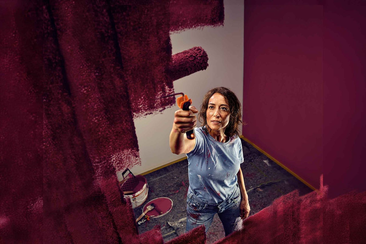 Een vrouw schildert een muur met een verfroller in een kamer.