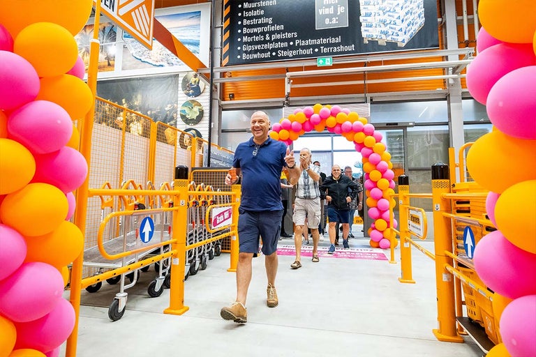 Een scène in een Hornbach filiaal met klanten en winkelwagens, versierd met ballonnen voor een feestelijke gelegenheid.