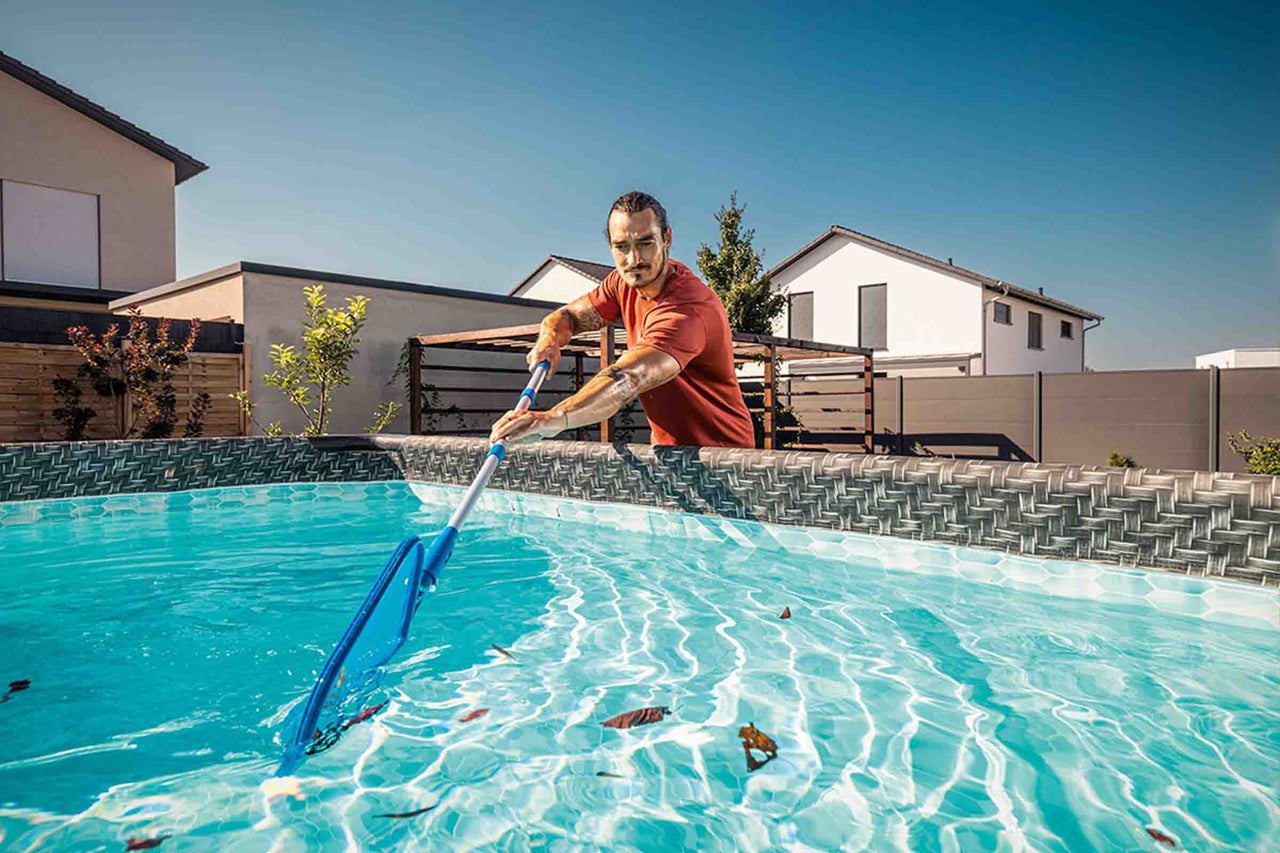 Een man maakt een opzetzwembad in de tuin schoon met een schepnet aan een telescoopstang.