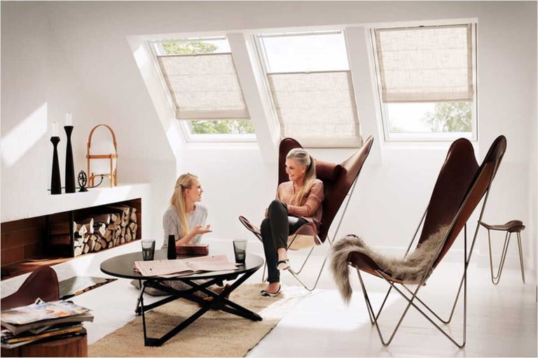 Lichte woonkamer met dakramen en rolgordijnen, ingericht met fauteuils en een salontafel.