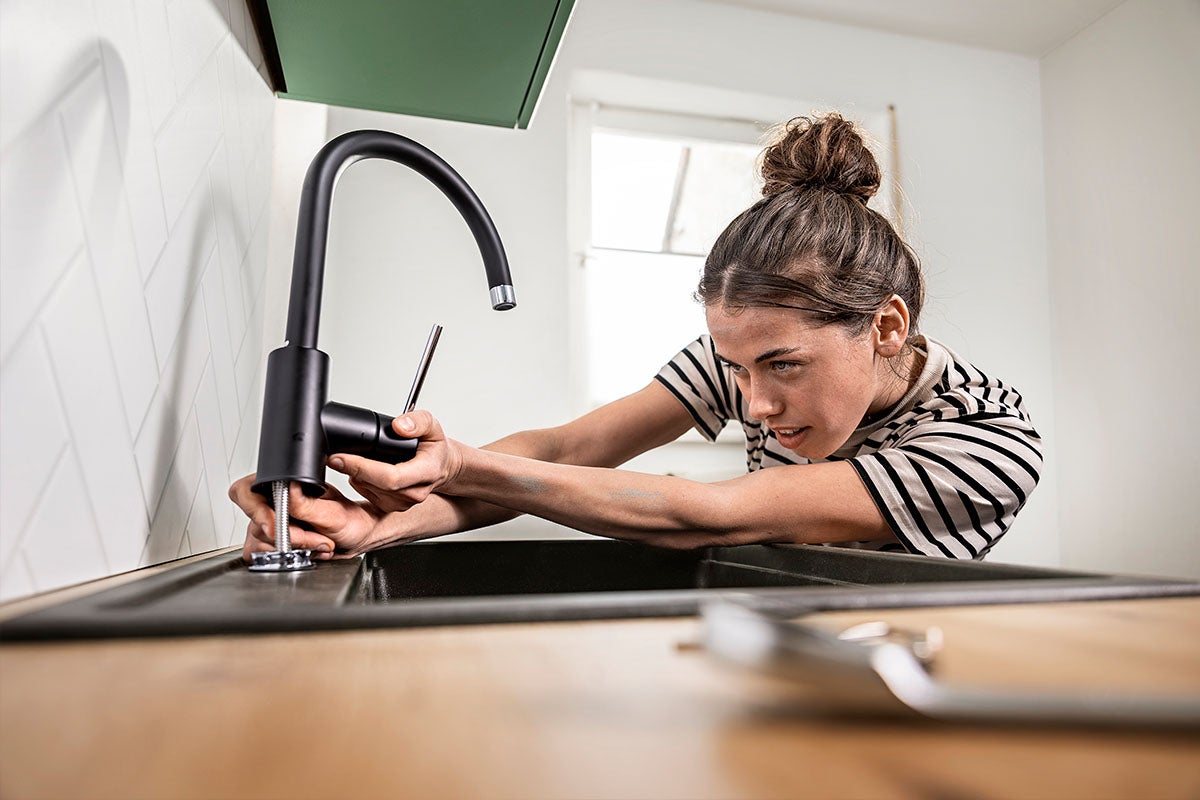 Een vrouw monteert een moderne keukenkraan op een gootsteen in de keuken.