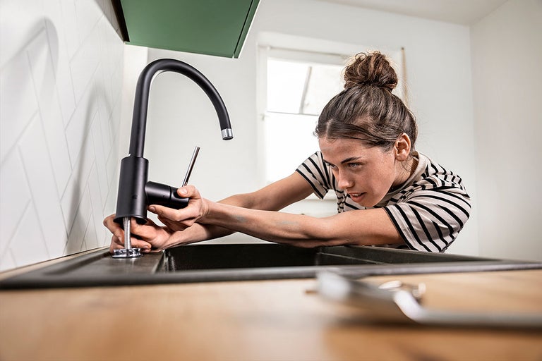 Een vrouw monteert een moderne keukenkraan op een gootsteen in de keuken.