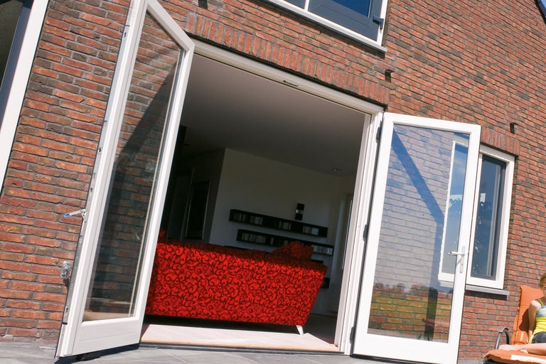 Openstaande terrasdeuren aan een bakstenen huis met uitzicht op een bank