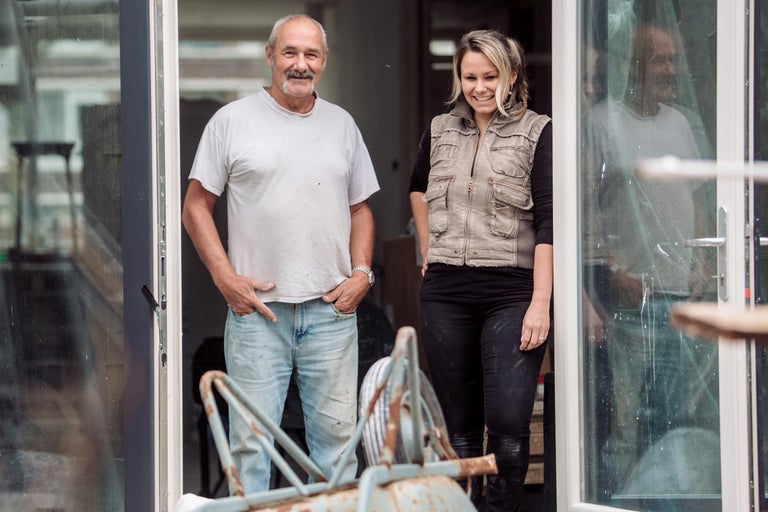 Twee mensen staan in een deuropening naast een kruiwagen.