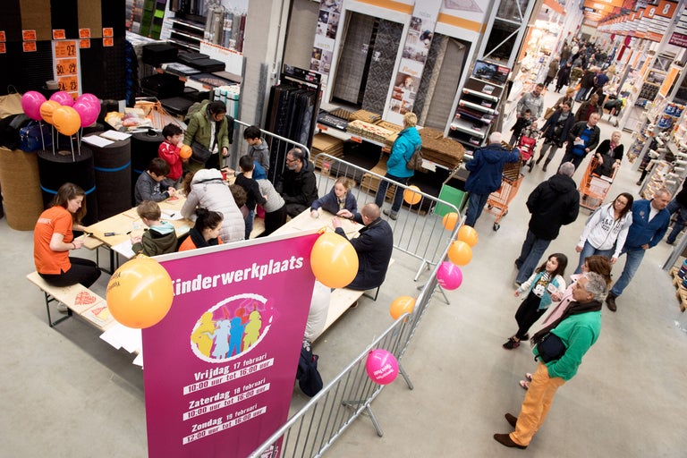 Een scène in een Hornbach-winkel met een kinderworkshop, waar kinderen aan tafels zitten te knutselen terwijl andere klanten door de winkel lopen.