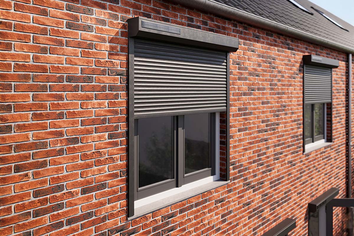 Rolluik met zonnepaneel gemonteerd op een rode bakstenen muur boven een raam.