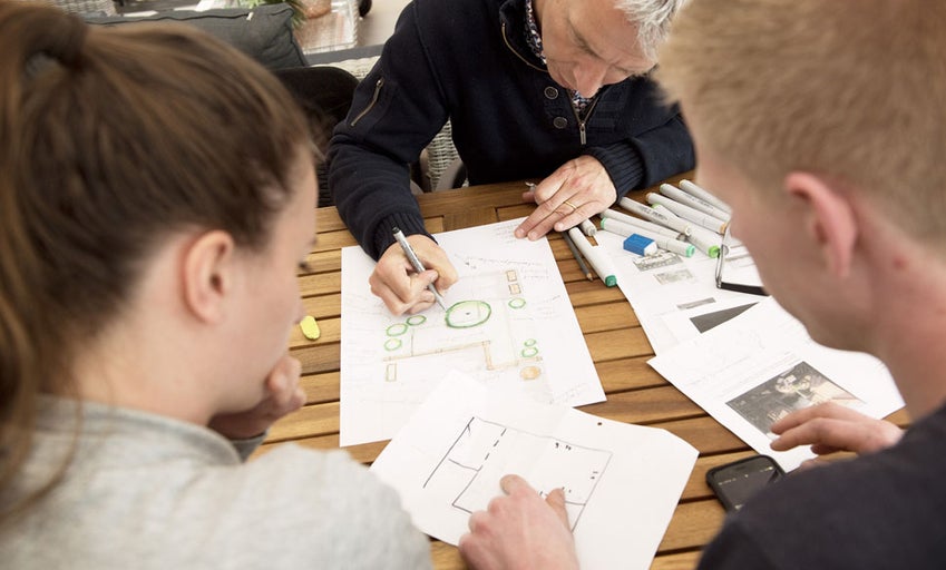 Mensen werken aan een tuinontwerp met pennen en stiften op een houten tafel.