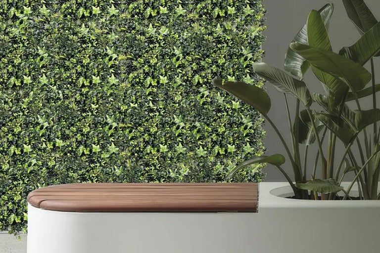 Decoratieve wand met kunstmatige klimop, zitbank met houten blad en kamerplant in een plantenbak.