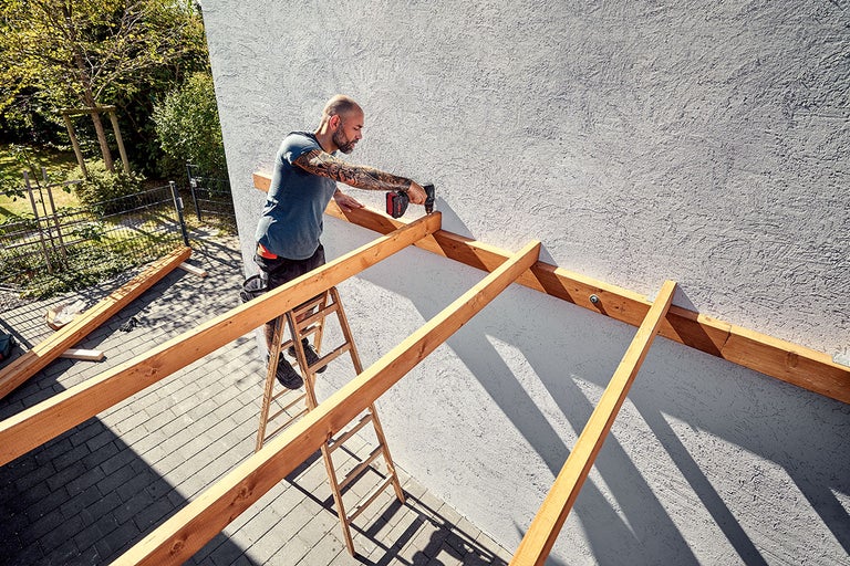 Man monteert houten constructie met accuschroevendraaier aan de muur van het huis.