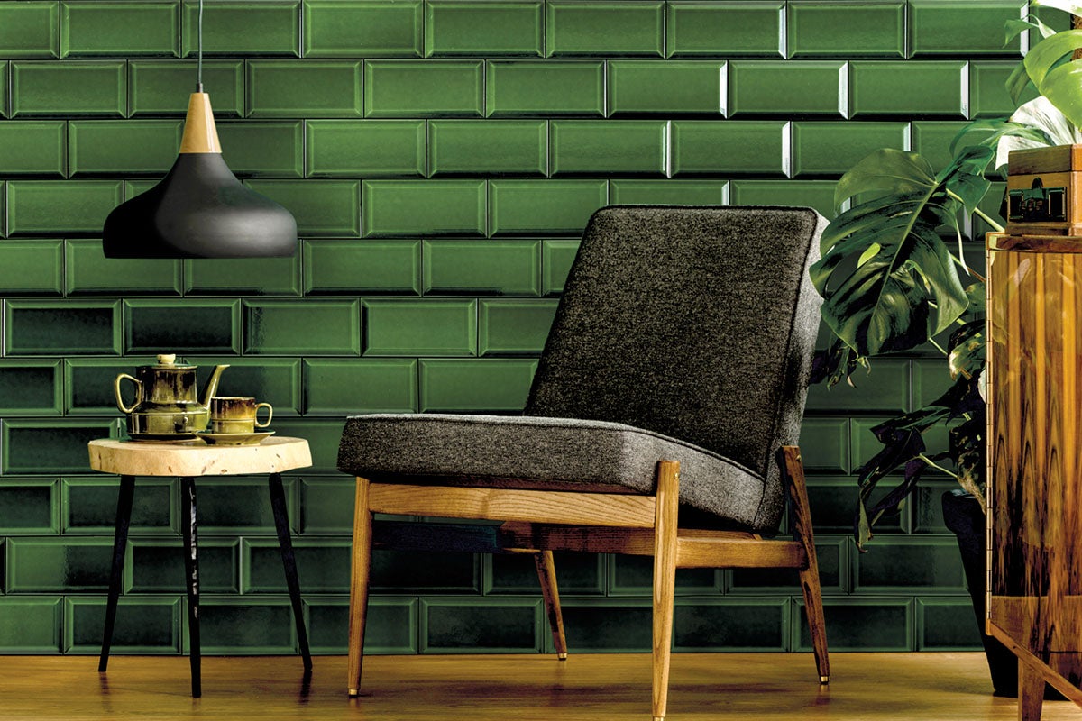 Woonkamer met groene metro tegels op de muur, een stoel, een bijzettafel en een hanglamp.