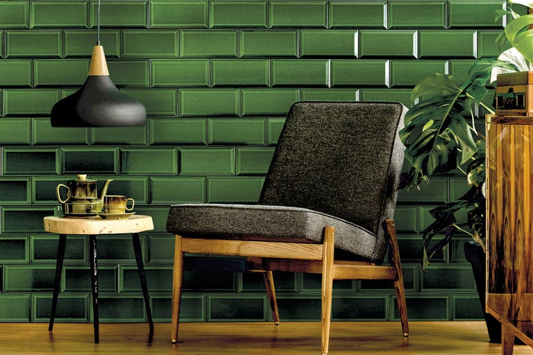 Woonkamer met groene metro tegels op de muur, een stoel, een bijzettafel en een hanglamp.