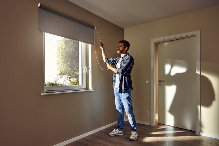 Man bedient een rolgordijn bij het raam in een kamer.