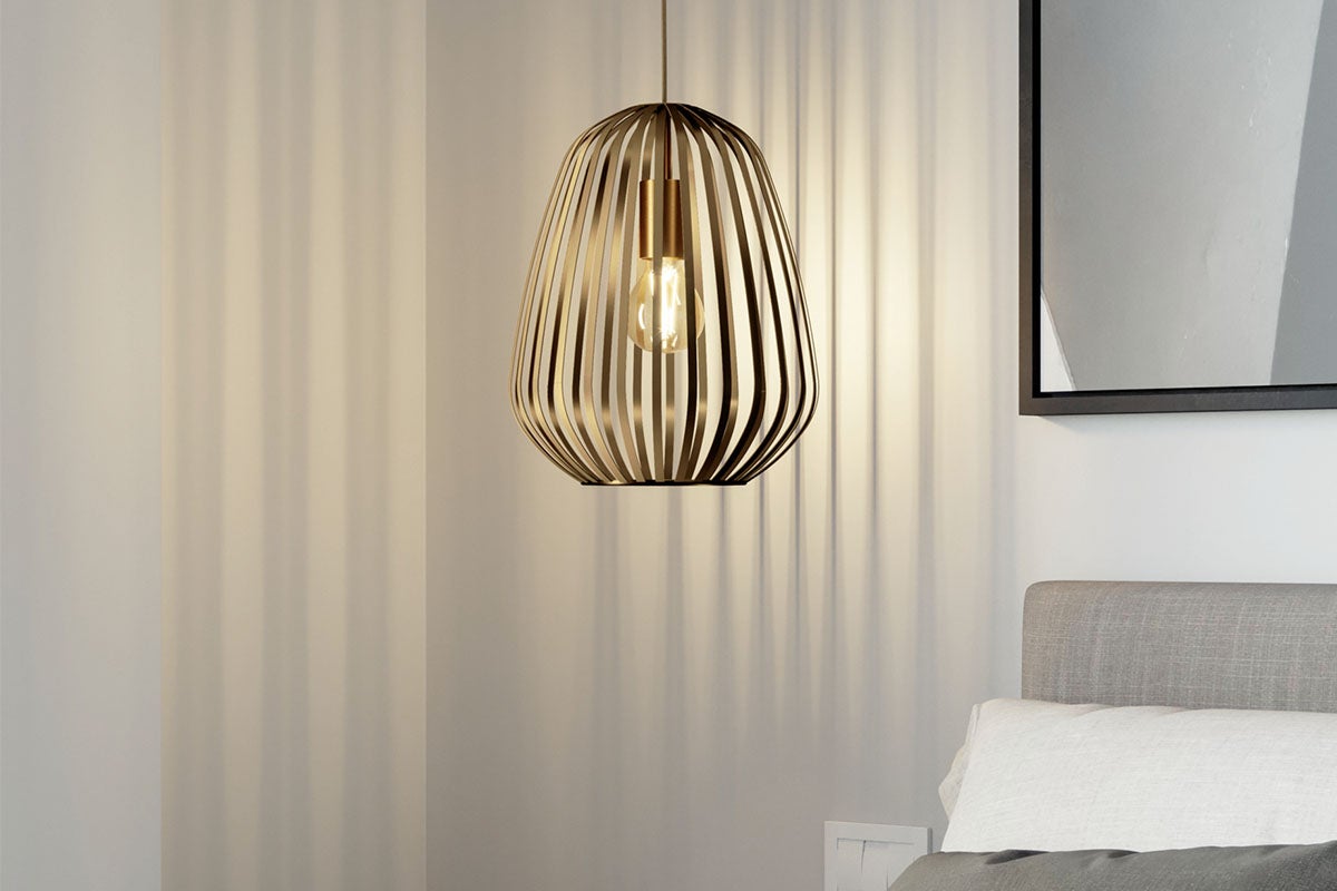 Moderne metalen hanglamp met een korfachtige lampenkap boven een bed in een lichte slaapkamer.