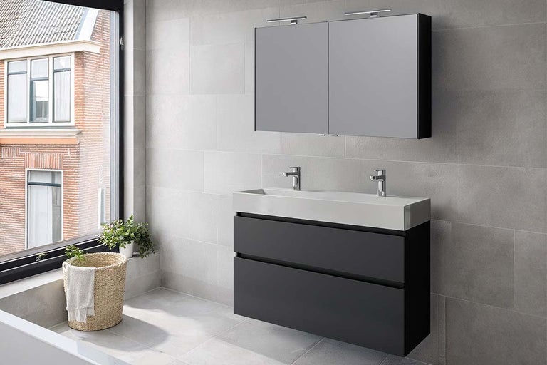 Moderne badkamer met donkergrijs dubbel wastafelmeubel, witte wastafel met twee kranen en een spiegelkast met verlichting.