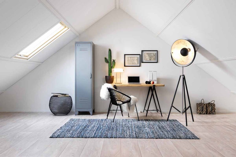 Zolderkamer met bureau, stoel, vloerlamp en blauw tapijt