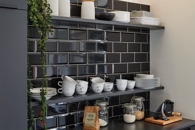 Planken met servies en levensmiddelen voor zwarte tegelwand in de keuken.