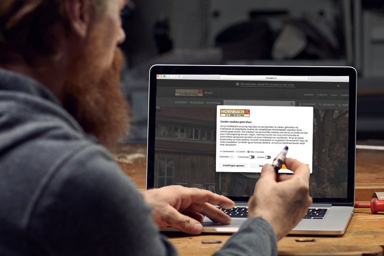 Een man met baard bedient een laptop waarop de Hornbach website met een cookiemelding wordt weergegeven.