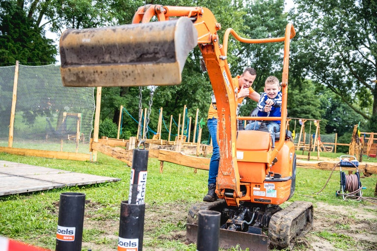 Vader en zoon bedienen een minigraver in de tuin.