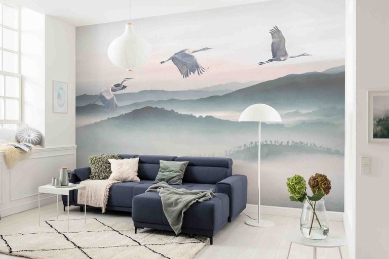Woonkamer met blauwe bank, patroonbehang met kraanvogels en berglandschap