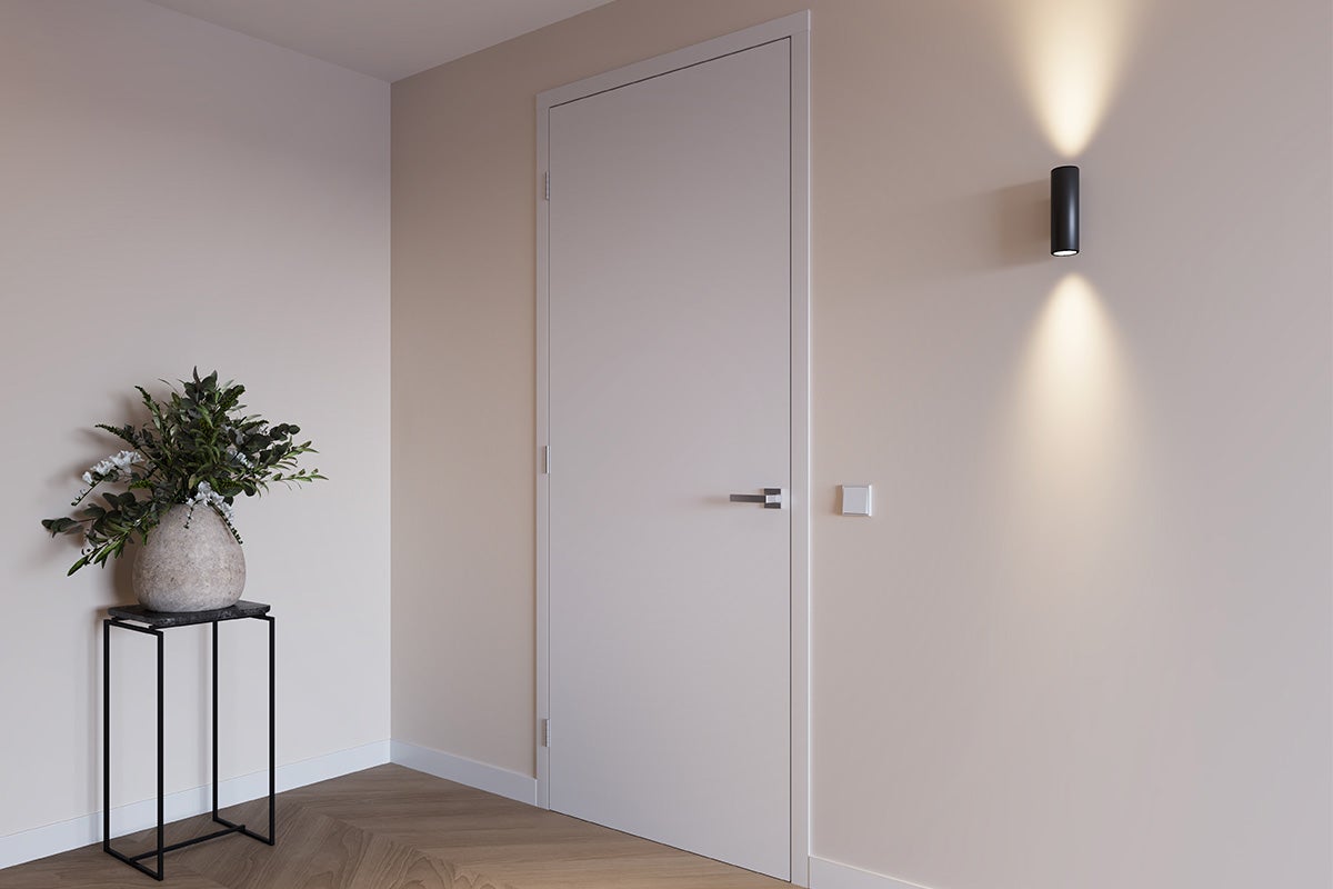 Lichte hal met binnendeur, wandlamp en bloemstuk op een bijzettafel.