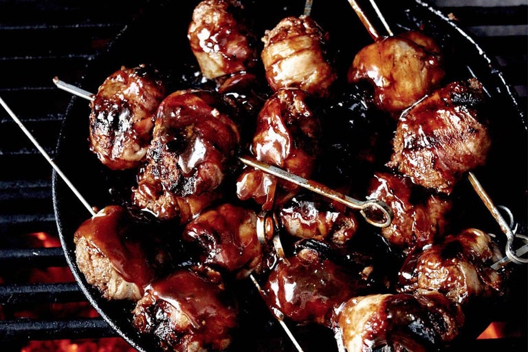 Vleesstukken op spiesen met saus op een barbecue.