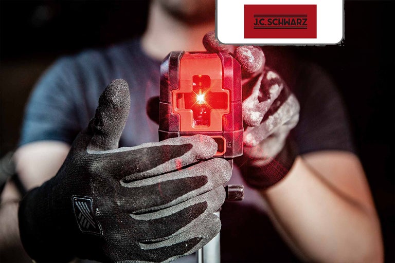 Hand met werkhandschoen houdt rood kruislijnlaserapparaat van het merk J.C. Schwarz vast