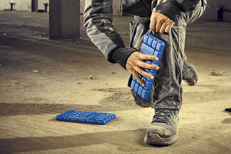 Man bevestigt kniebeschermer aan been. Een andere kniebeschermer ligt op de grond.