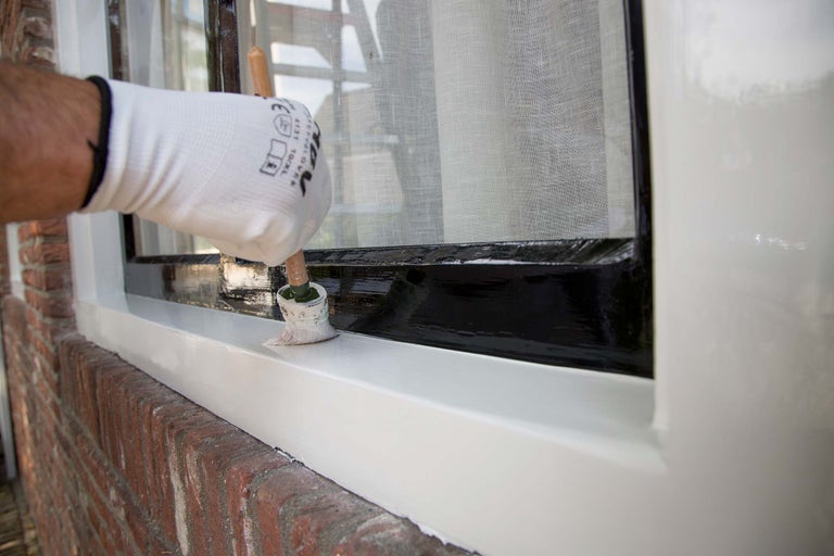 Persoon schildert een raam met een penseel en verf.