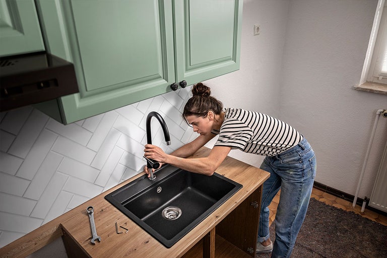 Een vrouw monteert een keukenkraan op een spoelbak in een keuken met gereedschap op het werkblad.