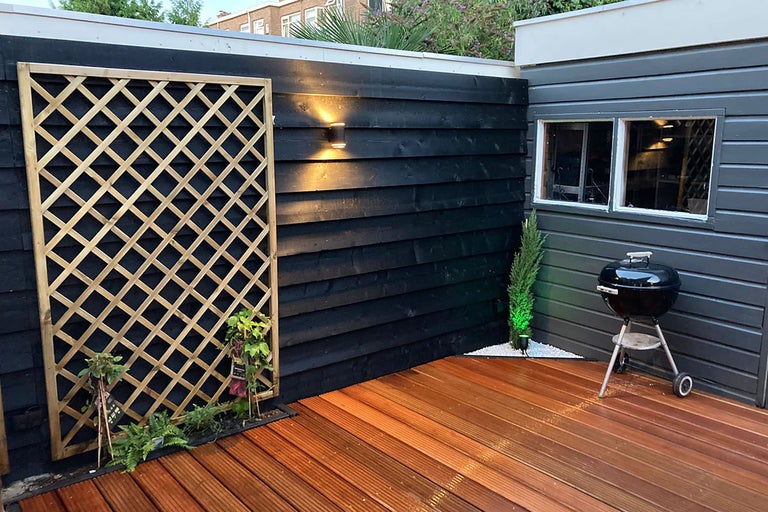 Aangelegde terras met houten vloer, houten wand, klimrek en barbecue
