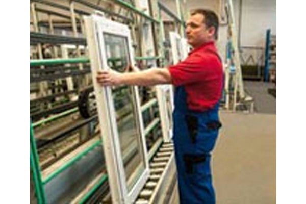 Een arbeider transporteert een kunststof raam in een fabriek.