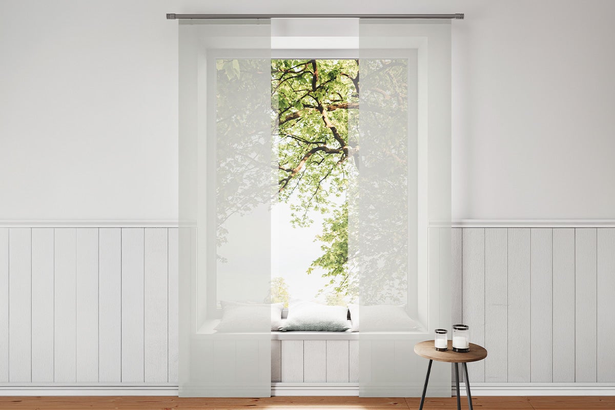 Witte transparante paneelgordijnen voor een raam in een lichte kamer met wandpanelen en een houten vloer.