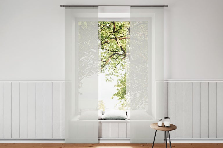 Witte transparante paneelgordijnen voor een raam in een lichte kamer met wandpanelen en een houten vloer.