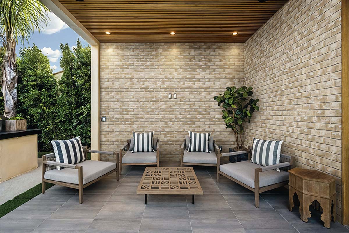 Steenstrips met baksteenlook op een buitenmuur in een lichte, modern ingerichte patio met loungemeubels en een houten plafond.