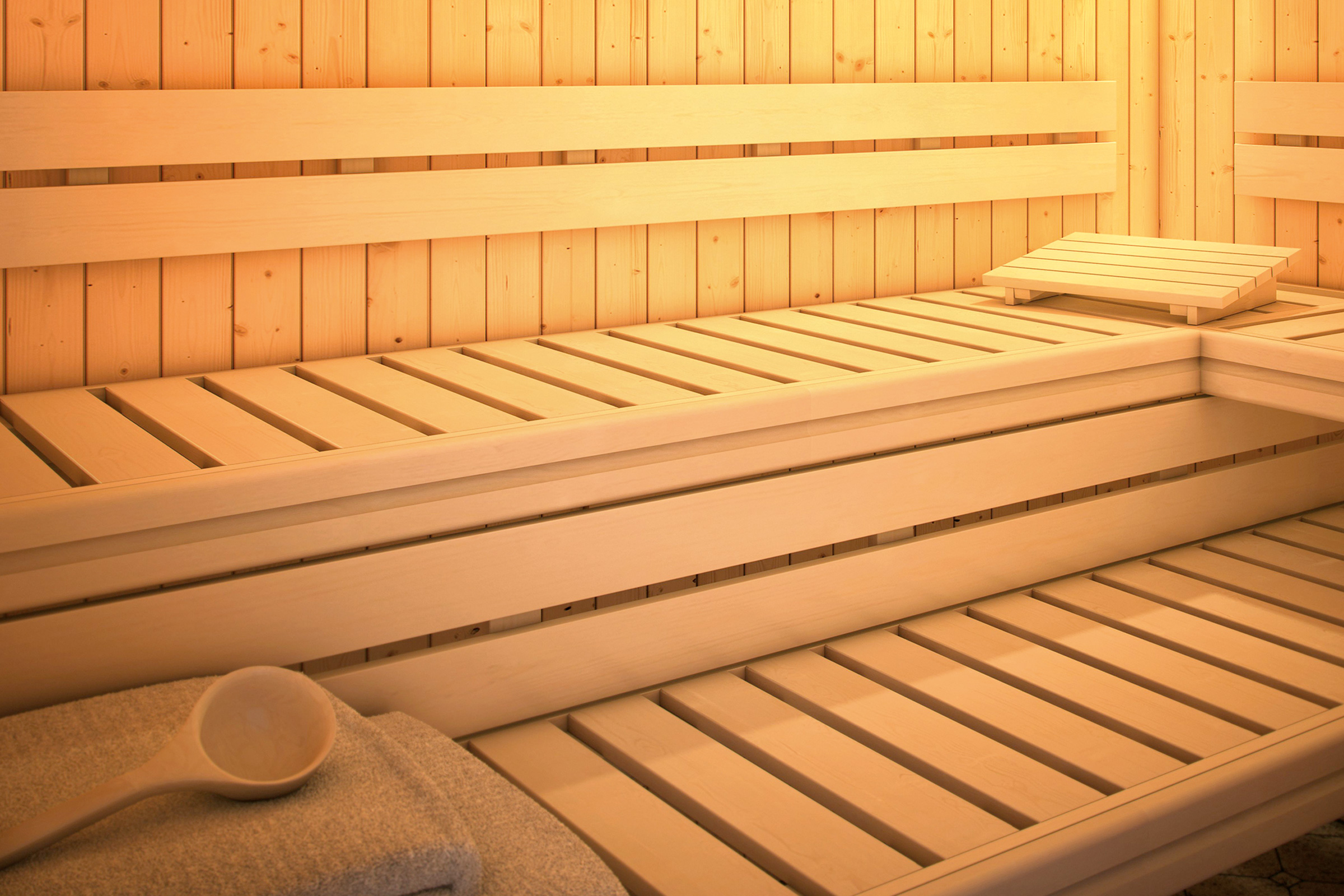 Sauna met houten banken, een hoofdsteun, een handdoek en een opscheplepel.