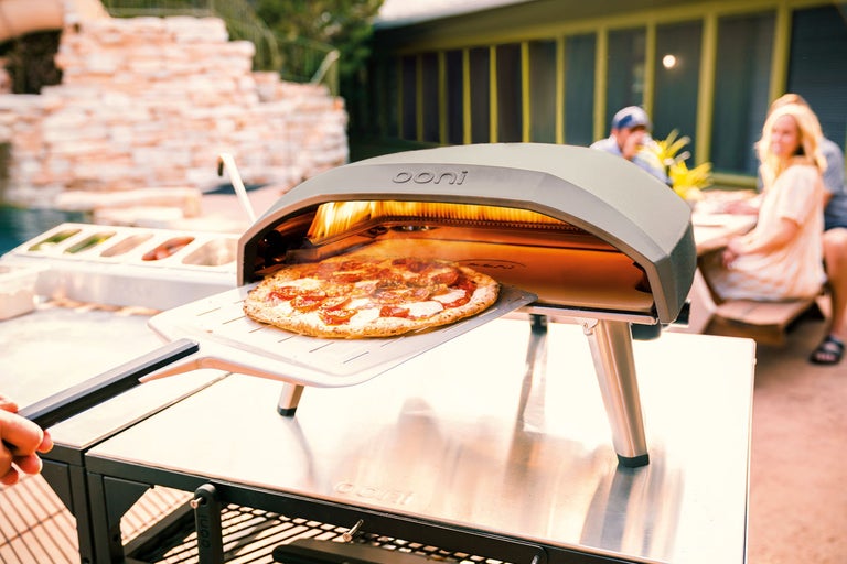 Ooni pizzaoven met pizza op pizzaschep buiten