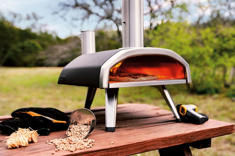 Pizzaoven met pizza, houtpellets, schep, ovenwanten en infraroodthermometer op een houten tafel buitenshuis